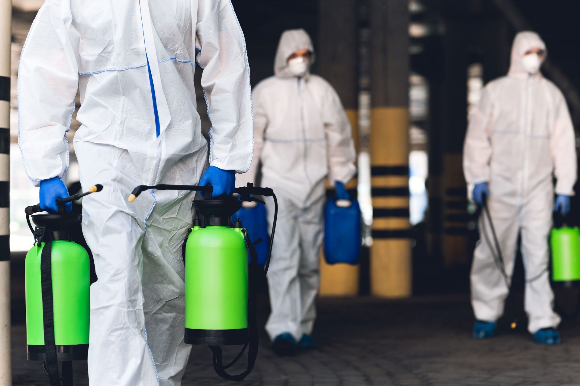 men in virus protective suits carrying spray bottles