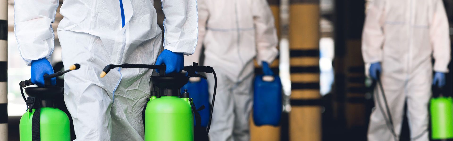 men in virus protective suits carrying spray bottles